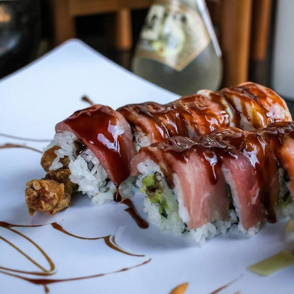 Two rows of sushi rolls topped with salmon and drizzled with sauce, served with ginger, wasabi, and decorative sauce on a white plate.